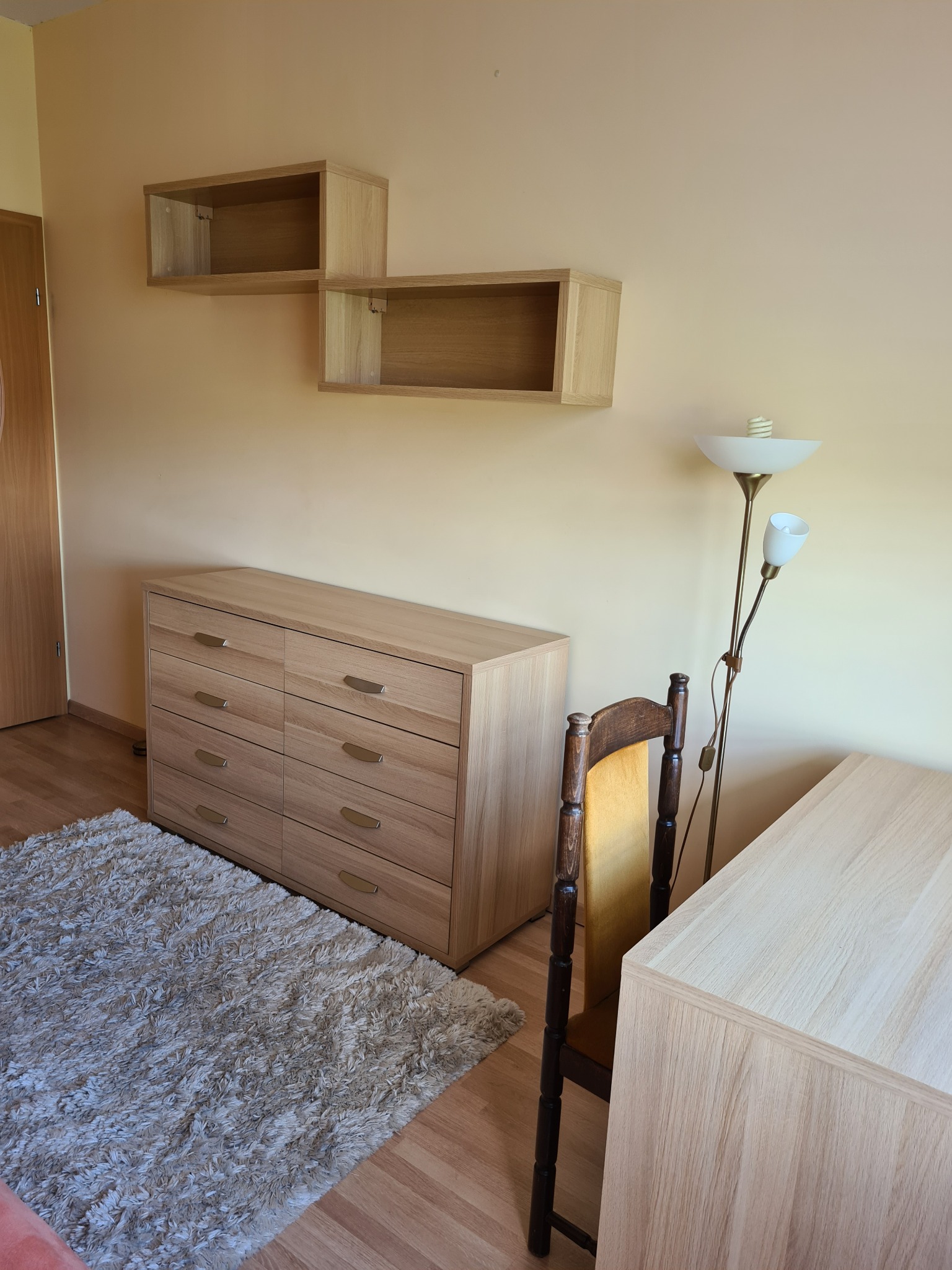 Pokój z komodą, półkami, biurkiem i lampą